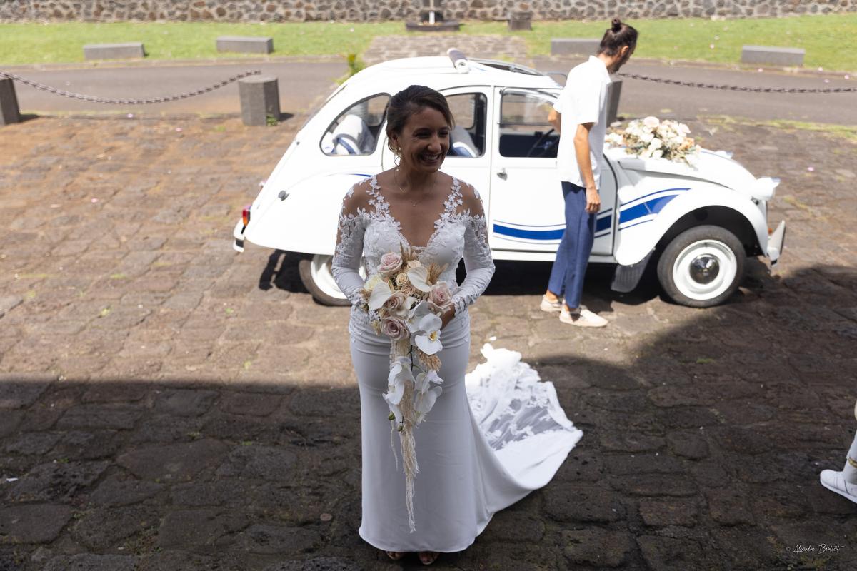 La mariée en robe blanche, bouquet à la main, devant la portière ouverte de la 2CV