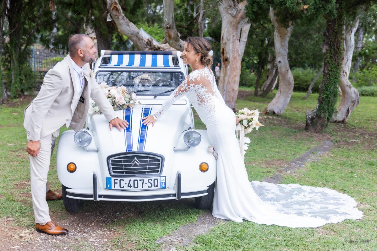 La mariée près de la 2CV fleurie, la traîne étalée sur l'herbe du jardin